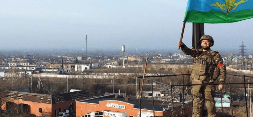 A Russian paratrooper raises a blue-and-green flag atop a structure in Suja city, after reported control was established in 2024.